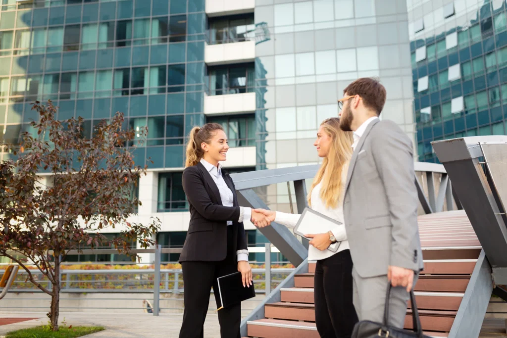 Three business people shaking hands in front of a building.