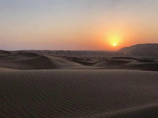 The sun is setting over a desert with sand dunes.