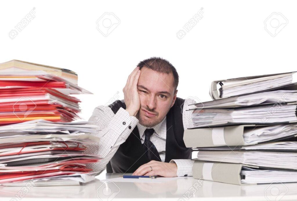 A businessman is sitting at his desk with a pile of papers on his head.