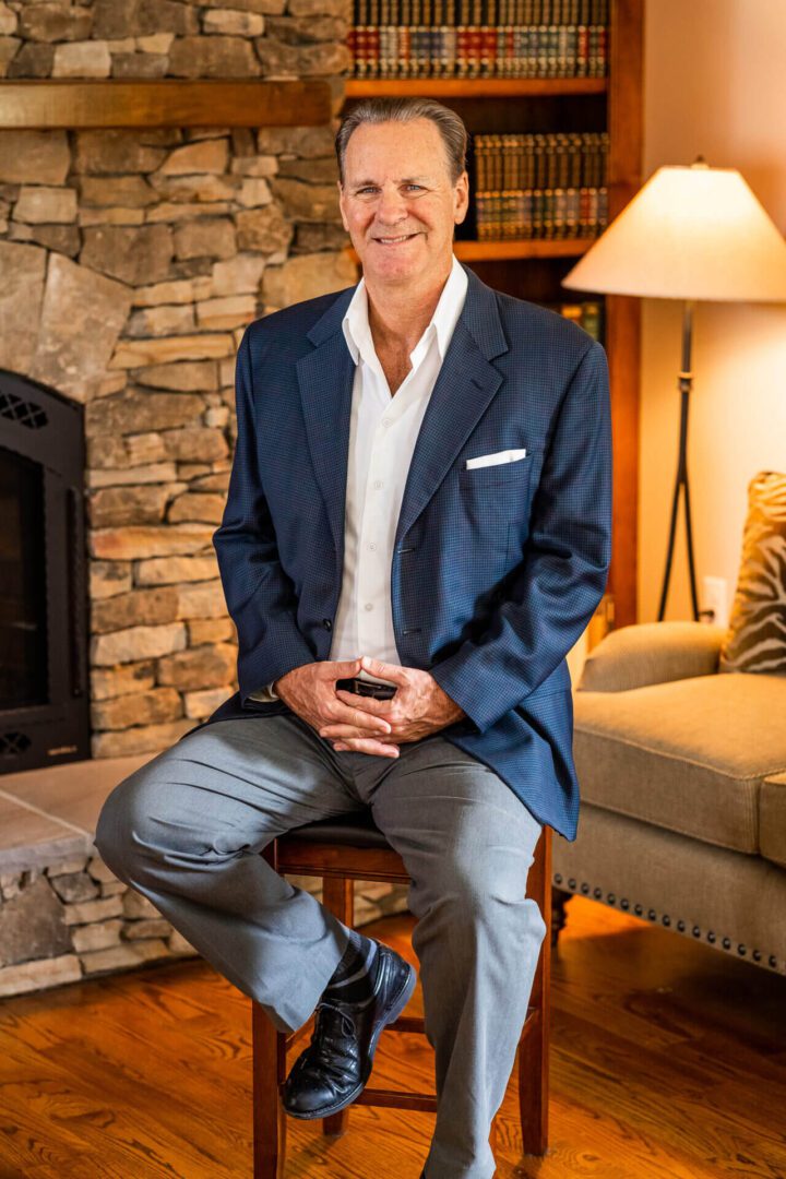 A man sitting on a chair in front of a fireplace.
