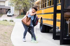 Two girls hugging in front of a school bus.
