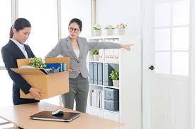 Two women in business suits moving boxes in an office.